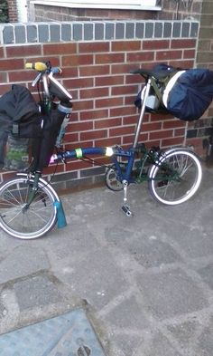 two bikes parked next to a brick wall with bags on the front and back rack