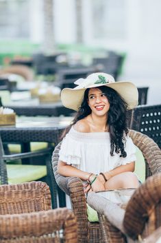 a woman wearing a white hat sitting on top of a wicker chair next to tables