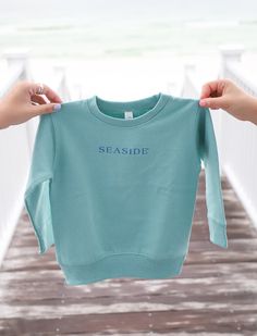 Our favorite SEASIDE® sweatshirt for your little one! Features SEASIDE® logo printed across the front beach baby on back. Casual Spring Sweatshirt For Playwear, Casual Sweatshirt With Ribbed Cuffs For Play, Casual Relaxed Fit Sweatshirt For Playwear, Casual Playwear Tops With Ribbed Cuffs, Ribbed Cuffs Crew Neck Sweatshirt For Playwear, Crew Neck Sweatshirt With Ribbed Cuffs For Playwear, Blue Crew Neck Sweatshirt For Playwear, Cotton Sweatshirt With Ribbed Cuffs For Playwear, Casual Blue Sweatshirt With Name Print