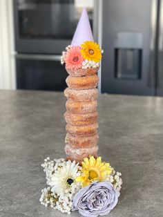 donuts are stacked on top of each other with flowers in front of the doughnut tower