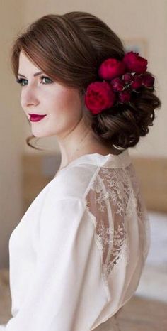 a woman with red flowers in her hair wearing a white blouse and holding a bouquet of roses