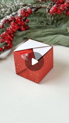 an origami box sitting on top of a white table next to holly branches