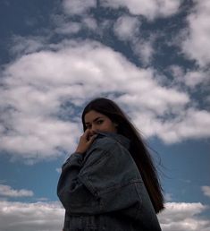 a woman standing in front of a blue sky with clouds on her head talking on a cell phone