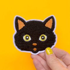 a hand holding a black cat patch with yellow eyes