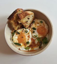 two fried eggs in a bowl with toast on the side and garnished with green leaves