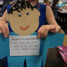 a young boy holding up a paper cut out of his face with writing on it