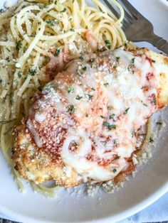 a white plate topped with chicken parmesan next to pasta and a fork on top of a table