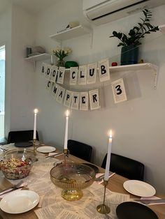 a dining room table set with plates, bowls and candles in front of the book club sign