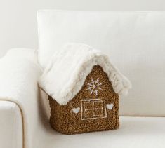 a gingerbread house pillow sitting on top of a white couch next to a white chair