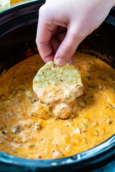 a hand dipping a tortilla chip into a slow cooker filled with cheese