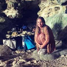 a man with long hair sitting on rocks next to a blue bag and water bottle