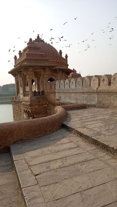 birds are flying over an old building by the water