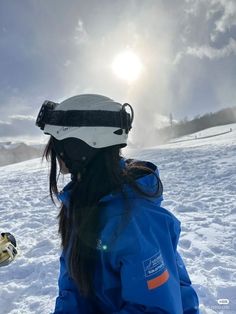 a woman sitting in the snow wearing a blue jacket and white ski goggles on her head