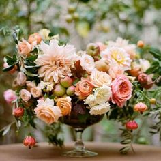 a vase filled with lots of flowers sitting on top of a table next to trees