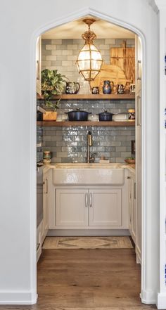 an open doorway leading to a kitchen with white cabinets and wooden shelves filled with dishes