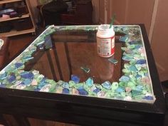 a glass table with sea glass on it and a paint can sitting on top of it