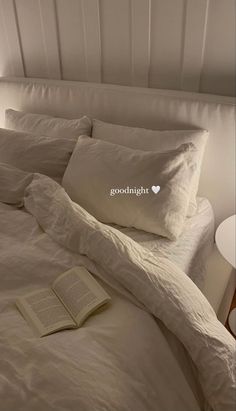 an open book is laying on the bed with white sheets and pillowcases, next to a lamp