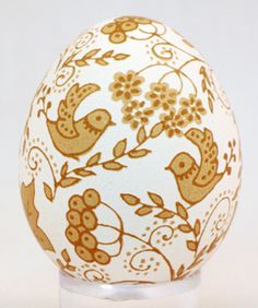 an egg decorated with birds and flowers on a clear base stands in front of a white background