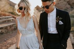 a man and woman in formal wear walking down a dirt road holding each other's hands