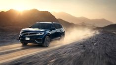 a blue suv driving down a dirt road with mountains in the backgrouund