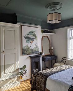 a bed sitting under a window next to a painting on the wall in a bedroom