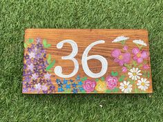 a wooden sign with flowers painted on it sitting in the grass next to a pair of scissors