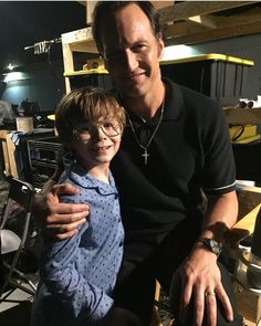 a man sitting next to a little boy on top of a wooden chair in a room