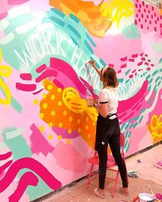 a woman is painting a large mural on the side of a building with pink and yellow flowers