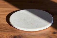 a white plate sitting on top of a wooden table next to a shadow from a window