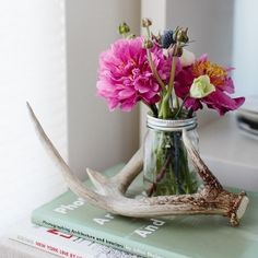 a vase filled with pink flowers sitting on top of a book next to a deer antler