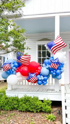 an american flag balloon arch on the front porch of a white house with red, white and blue balloons