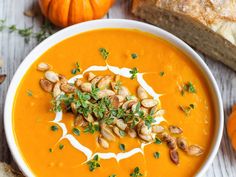 a white bowl filled with carrot soup next to bread and pumpkins on a table