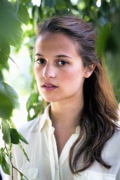 a woman standing under a tree with her hair pulled back and looking at the camera