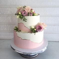 a three tiered cake with pink and white flowers on the top, sitting on a plate