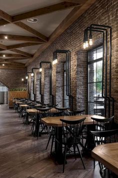 an empty restaurant with wooden tables and black metal chairs, brick walls and exposed beams