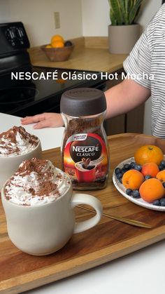 two mugs filled with whipped cream and oranges on a wooden tray next to a jar of nectarine