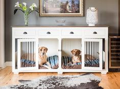 two dogs sitting in their kennels on top of a wooden floor next to a painting