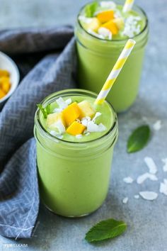 two glasses filled with green smoothie on top of a blue cloth and some leaves