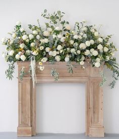 a mantel with white flowers and greenery on the top, along with green leaves