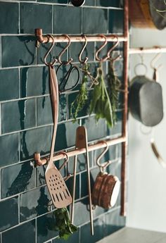 pots and pans are hanging on a rack in the kitchen with green tiles behind them