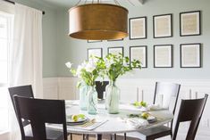 a dining room table and chairs with flowers in vases on the table next to it