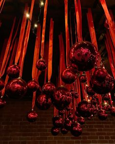 red balls and ribbons hanging from the ceiling in front of a brick wall with lights