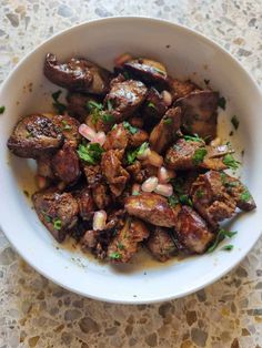 a white bowl filled with meat and garnish on top of a marble table