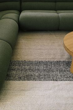 a green couch sitting on top of a rug next to a wooden table