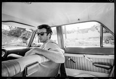 a man sitting in the back seat of a car with his arms folded out and wearing sunglasses