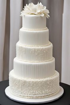 a three tiered white wedding cake with pearls and a flower on the top layer