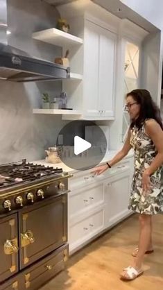 a woman standing in front of an oven with her hand on the stove top and pointing at it