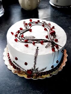 a white cake decorated with red berries and beads on a black table next to a teapot