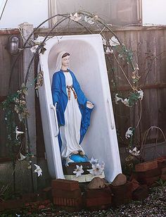 a statue of the virgin mary in a bathtub with flowers around it and vines