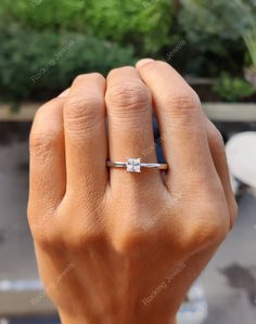 a woman's hand with a diamond ring on her finger, in front of some plants